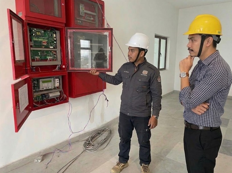 Engineers inspecting fire alarm control panels on a commercial site